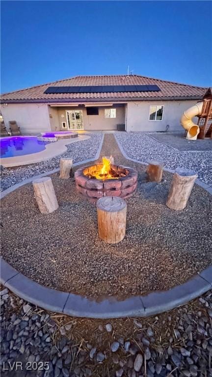 rear view of property featuring solar panels and a fire pit