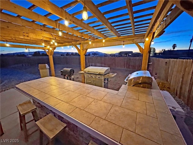 patio terrace at dusk with an outdoor kitchen, grilling area, and a pergola