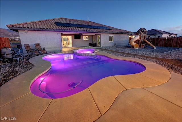 pool at dusk featuring a playground, central AC unit, an in ground hot tub, and a patio