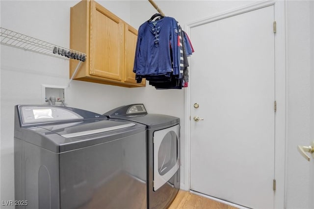 clothes washing area with light hardwood / wood-style flooring, separate washer and dryer, and cabinets