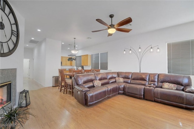 living room featuring ceiling fan, a tile fireplace, and light hardwood / wood-style flooring