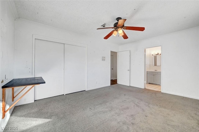 unfurnished bedroom with light carpet, ensuite bathroom, ceiling fan, a closet, and a textured ceiling