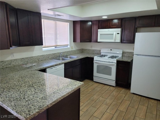 kitchen with light stone countertops, sink, white appliances, and kitchen peninsula