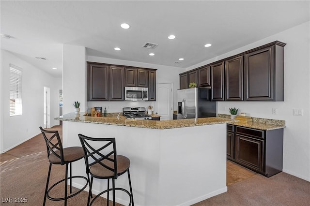 kitchen featuring light carpet, a kitchen bar, kitchen peninsula, stainless steel appliances, and light stone counters