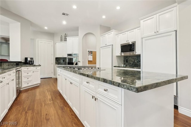 kitchen featuring tasteful backsplash, built in appliances, dark wood-type flooring, white cabinets, and dark stone counters