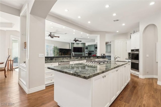 kitchen with a large island with sink, white cabinetry, stainless steel appliances, dark stone countertops, and backsplash