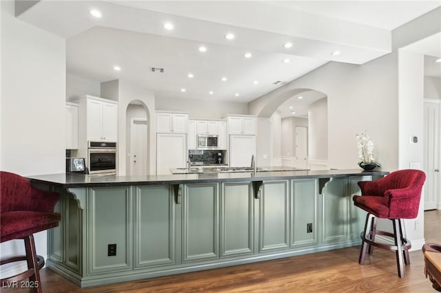 kitchen featuring white cabinetry, kitchen peninsula, appliances with stainless steel finishes, backsplash, and a kitchen breakfast bar