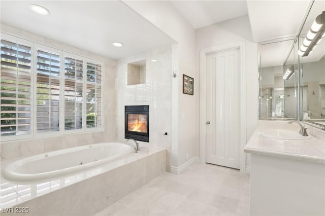 bathroom featuring vanity, a large fireplace, a wealth of natural light, and tiled tub