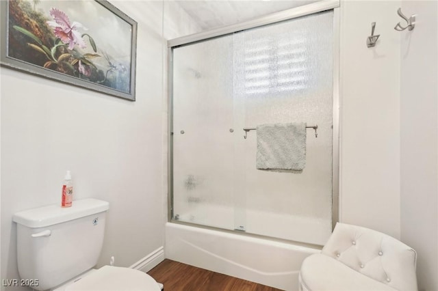 bathroom with hardwood / wood-style flooring, shower / bath combination with glass door, and toilet