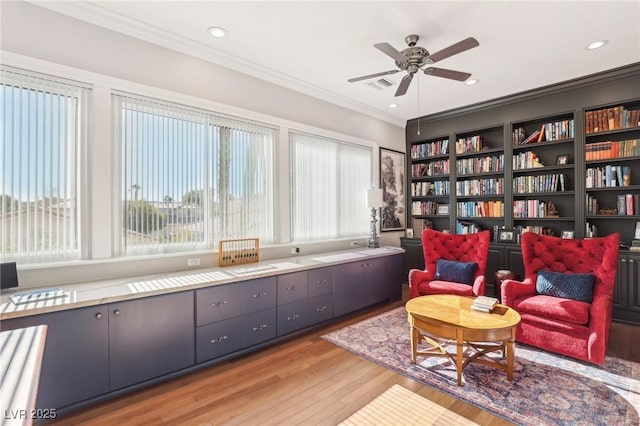 living area with ceiling fan, a wealth of natural light, ornamental molding, and light hardwood / wood-style flooring