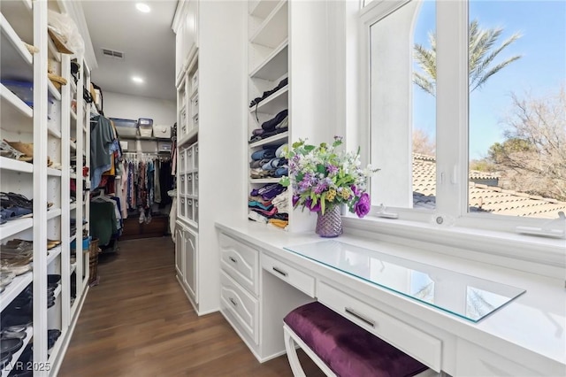 spacious closet with built in desk and dark hardwood / wood-style floors