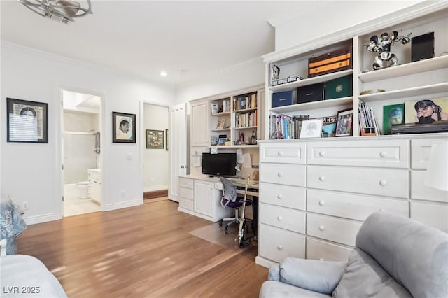 office area with light wood-type flooring, ornamental molding, and built in desk