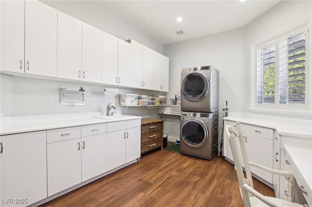 laundry room featuring cabinets, dark wood-type flooring, stacked washer / drying machine, and sink