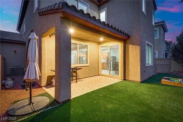 back house at dusk featuring a lawn, cooling unit, and a patio