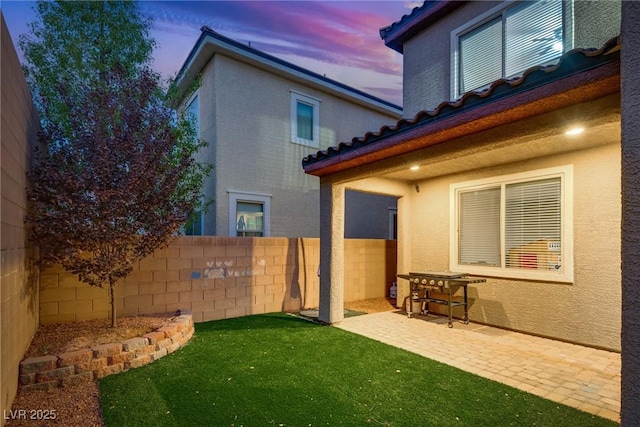 back house at dusk featuring a lawn and a patio