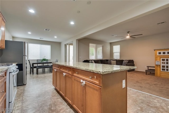 kitchen with light carpet, a healthy amount of sunlight, light stone counters, white gas range oven, and a center island