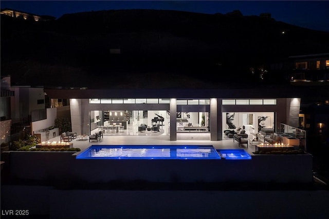 pool at night with a fire pit and a patio