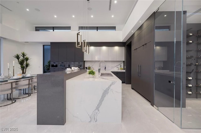 kitchen featuring decorative backsplash, a kitchen island with sink, decorative light fixtures, a towering ceiling, and sink