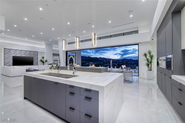 kitchen featuring light stone counters, sink, a large island with sink, and gray cabinetry