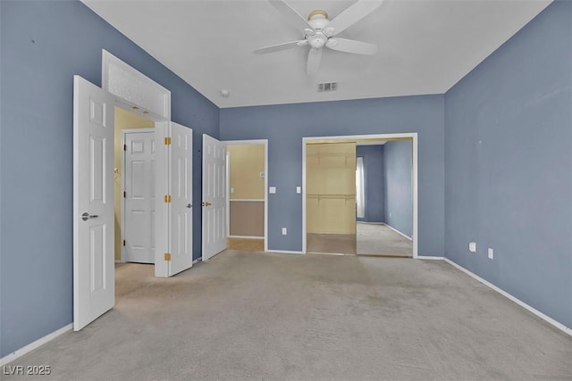 unfurnished bedroom featuring a walk in closet, light colored carpet, a closet, and ceiling fan