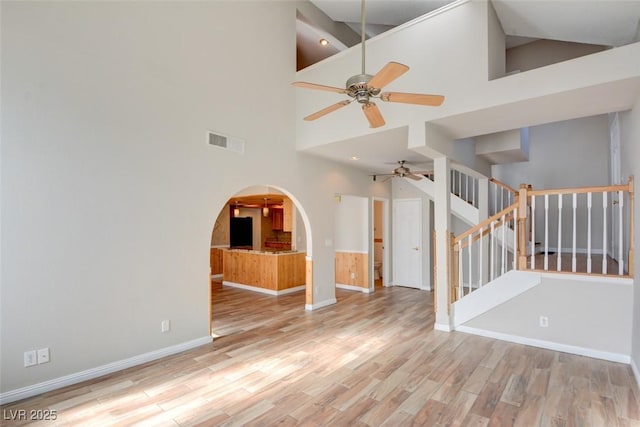 empty room featuring ceiling fan, a towering ceiling, and light hardwood / wood-style floors