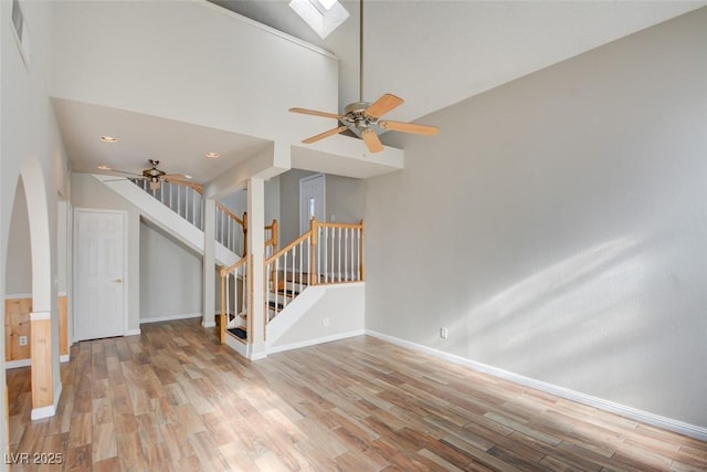 unfurnished living room with a skylight, light hardwood / wood-style flooring, and high vaulted ceiling