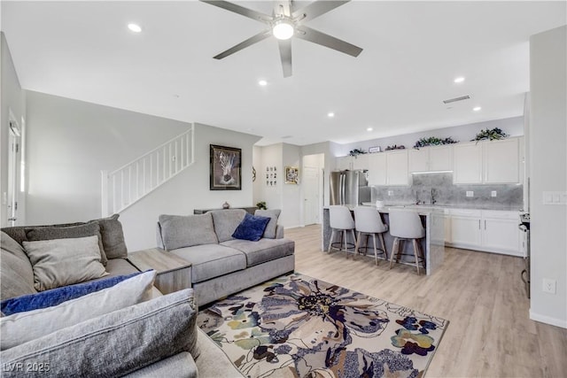 living room featuring ceiling fan, sink, and light wood-type flooring