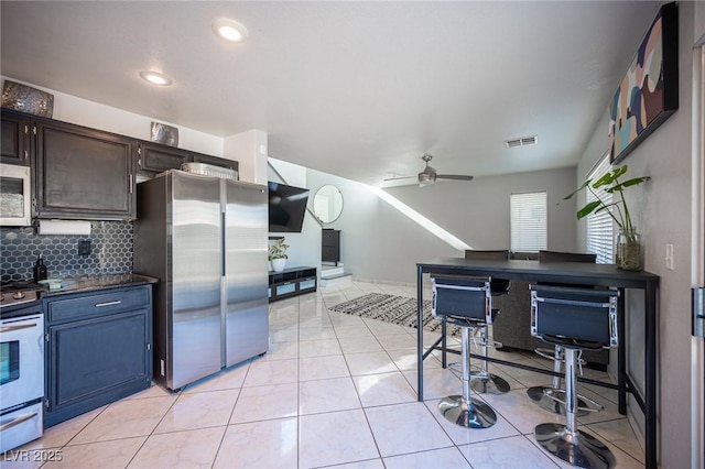 kitchen featuring dark brown cabinets, ceiling fan, appliances with stainless steel finishes, backsplash, and light tile patterned floors