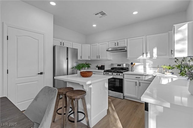 kitchen with light hardwood / wood-style flooring, white cabinets, a kitchen bar, a center island, and stainless steel appliances