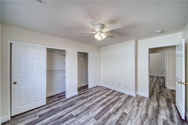 unfurnished bedroom with ceiling fan, dark hardwood / wood-style flooring, and multiple closets