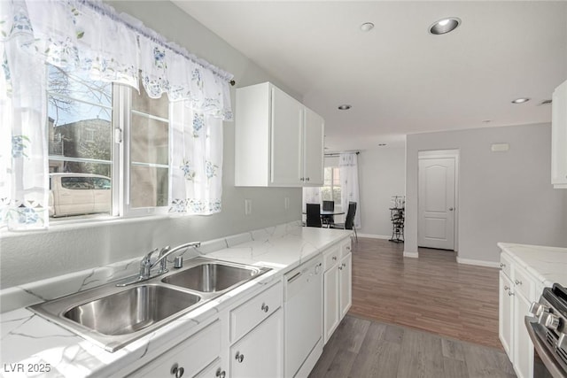 kitchen featuring stainless steel stove, dishwasher, wood-type flooring, sink, and white cabinets