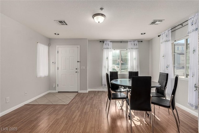 dining space featuring a healthy amount of sunlight, a textured ceiling, and light hardwood / wood-style floors