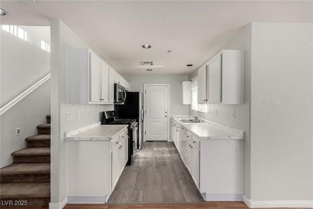 kitchen featuring sink, hardwood / wood-style flooring, white cabinetry, stainless steel appliances, and light stone counters