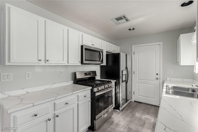 kitchen with white cabinetry, stainless steel appliances, and light stone counters