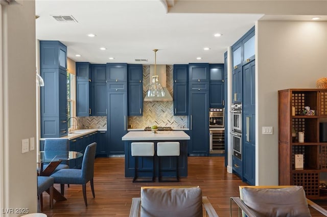 kitchen with blue cabinetry, hanging light fixtures, and wall chimney range hood