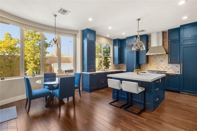 kitchen featuring wall chimney range hood, decorative light fixtures, a center island, and blue cabinetry