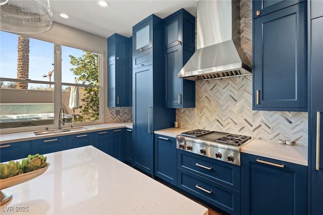 kitchen featuring wall chimney exhaust hood, sink, backsplash, blue cabinets, and stainless steel gas cooktop