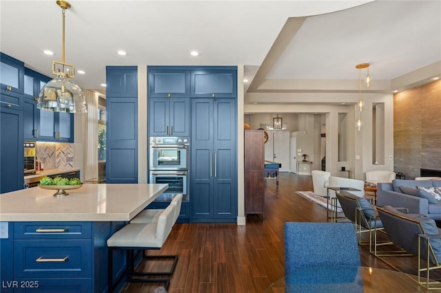 kitchen with decorative light fixtures, blue cabinetry, stainless steel double oven, and a kitchen bar