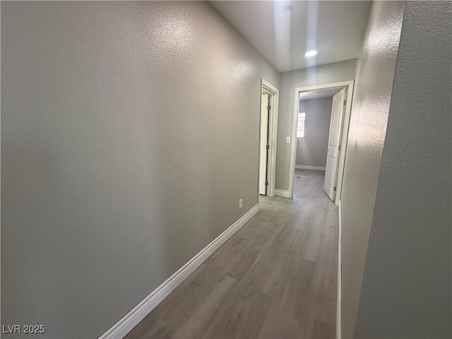 hallway with a textured wall, baseboards, and wood finished floors