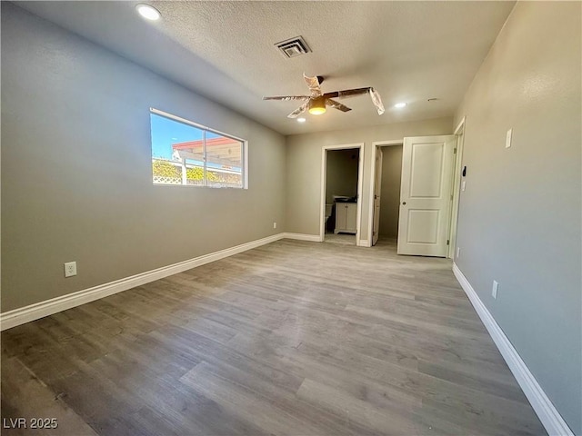 unfurnished bedroom featuring a textured ceiling, wood finished floors, visible vents, and baseboards