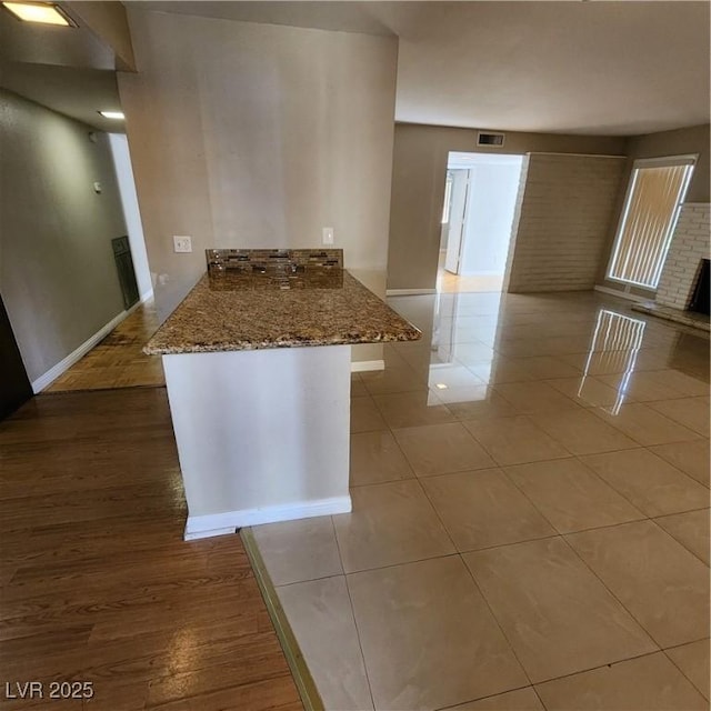 kitchen with a brick fireplace, kitchen peninsula, light tile patterned floors, and stone counters