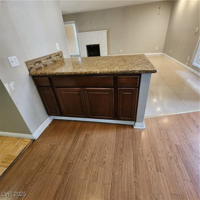 kitchen with dark brown cabinets, light wood-type flooring, a brick fireplace, and light stone countertops