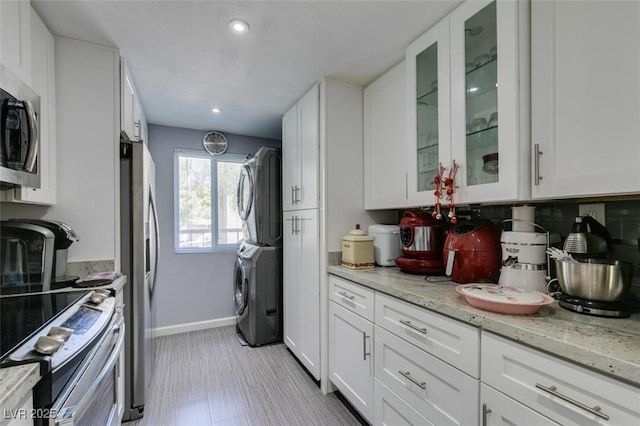 kitchen with light stone countertops, white cabinets, stacked washer and clothes dryer, backsplash, and stainless steel appliances