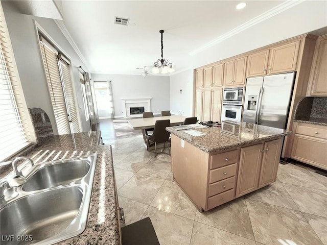 kitchen featuring a kitchen island, decorative light fixtures, stainless steel appliances, dark stone countertops, and sink