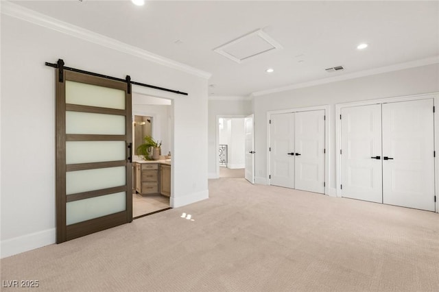 unfurnished bedroom featuring multiple closets, ensuite bath, a barn door, ornamental molding, and light colored carpet