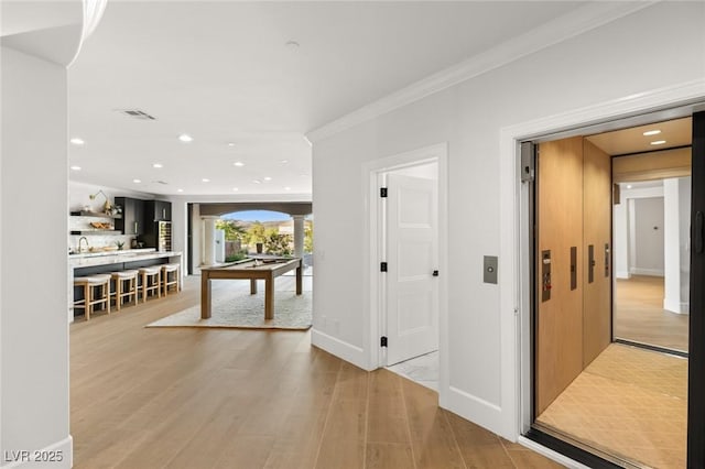 corridor with crown molding, light wood-type flooring, sink, and ornate columns