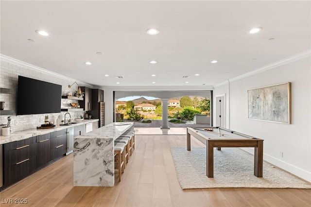 playroom featuring decorative columns, indoor wet bar, crown molding, and light wood-type flooring