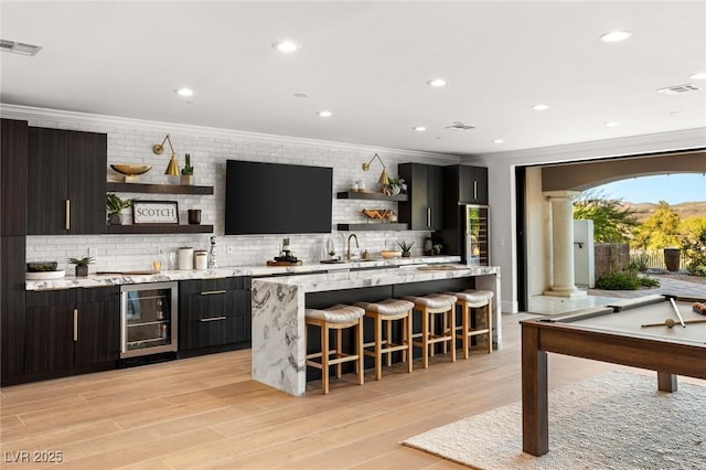 bar featuring sink, backsplash, light stone countertops, ornamental molding, and beverage cooler