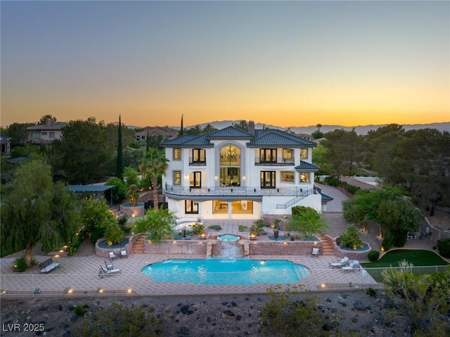 back house at dusk with a balcony, pool water feature, and a patio