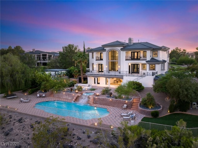 back house at dusk with a pool with hot tub and a patio